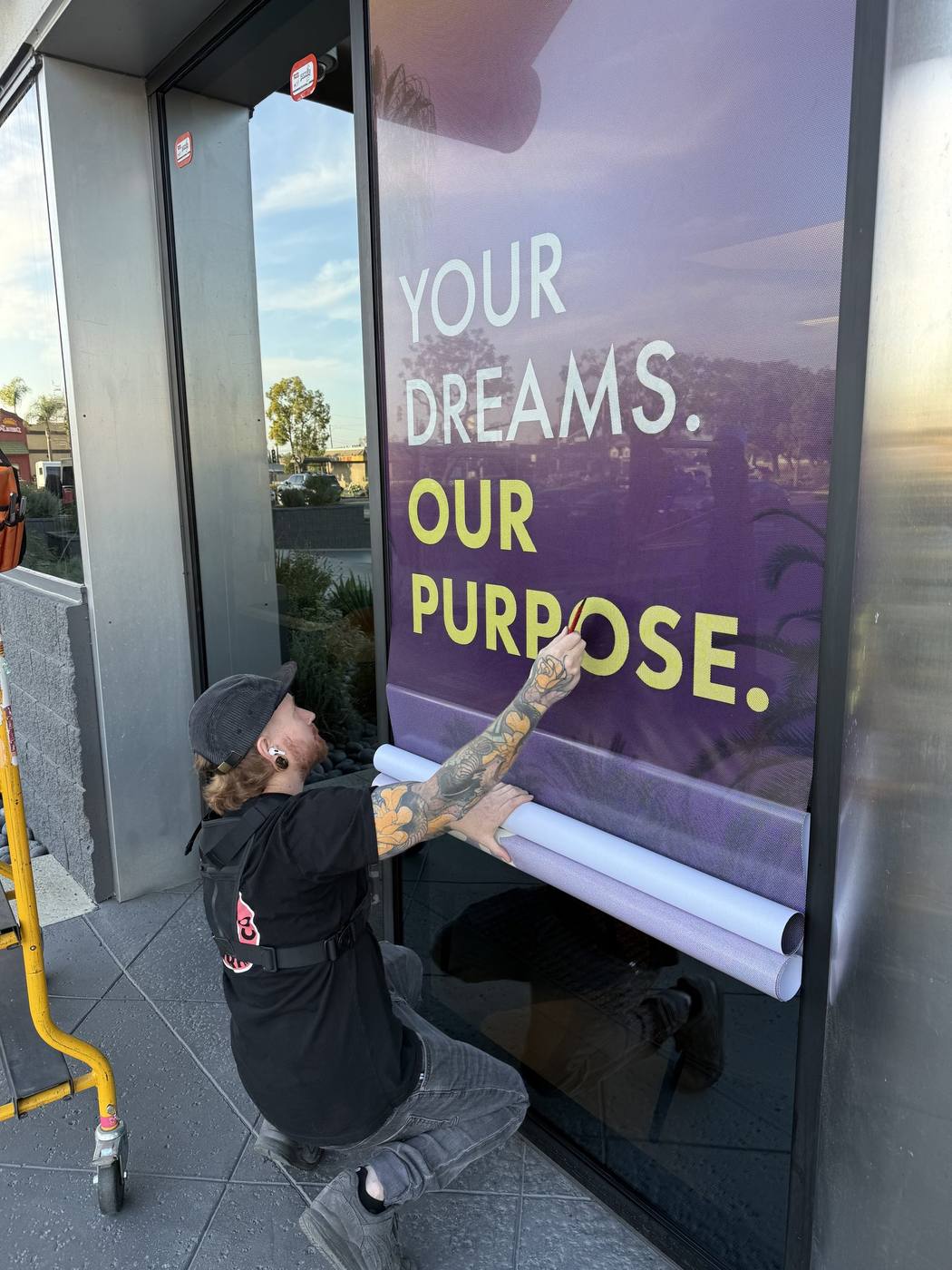 Kinetic Print Co installer applying a Rize window graphic reading Your Dreams Our Purpose
