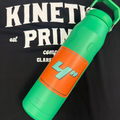 An orange 4 inch square sticker on a green watter bottle laying on t-shirt that says Kinetic Print Co