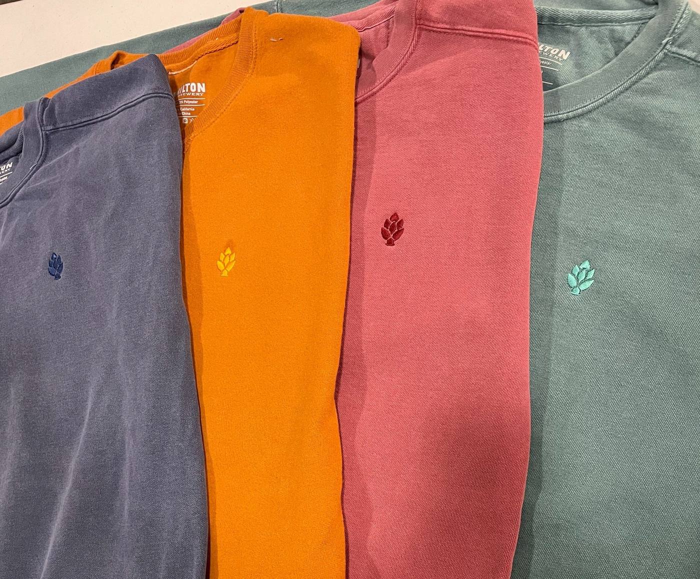 Stack of embroidered t-shirts in four colours with a small chest logo