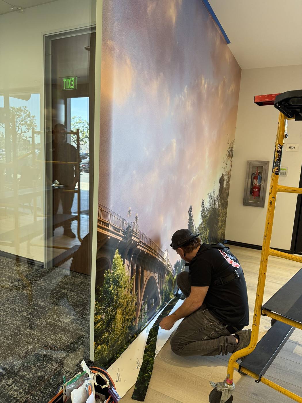 Installer applying a large Colorado Street Bridge scenic wall mural inside an office