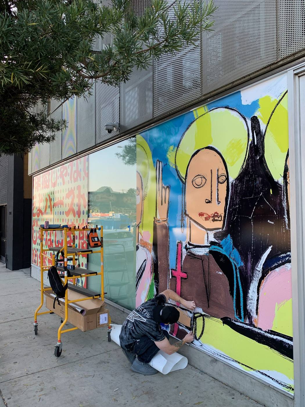 Kinetic Print Co installer applying a colourful figurative art window mural across a storefront